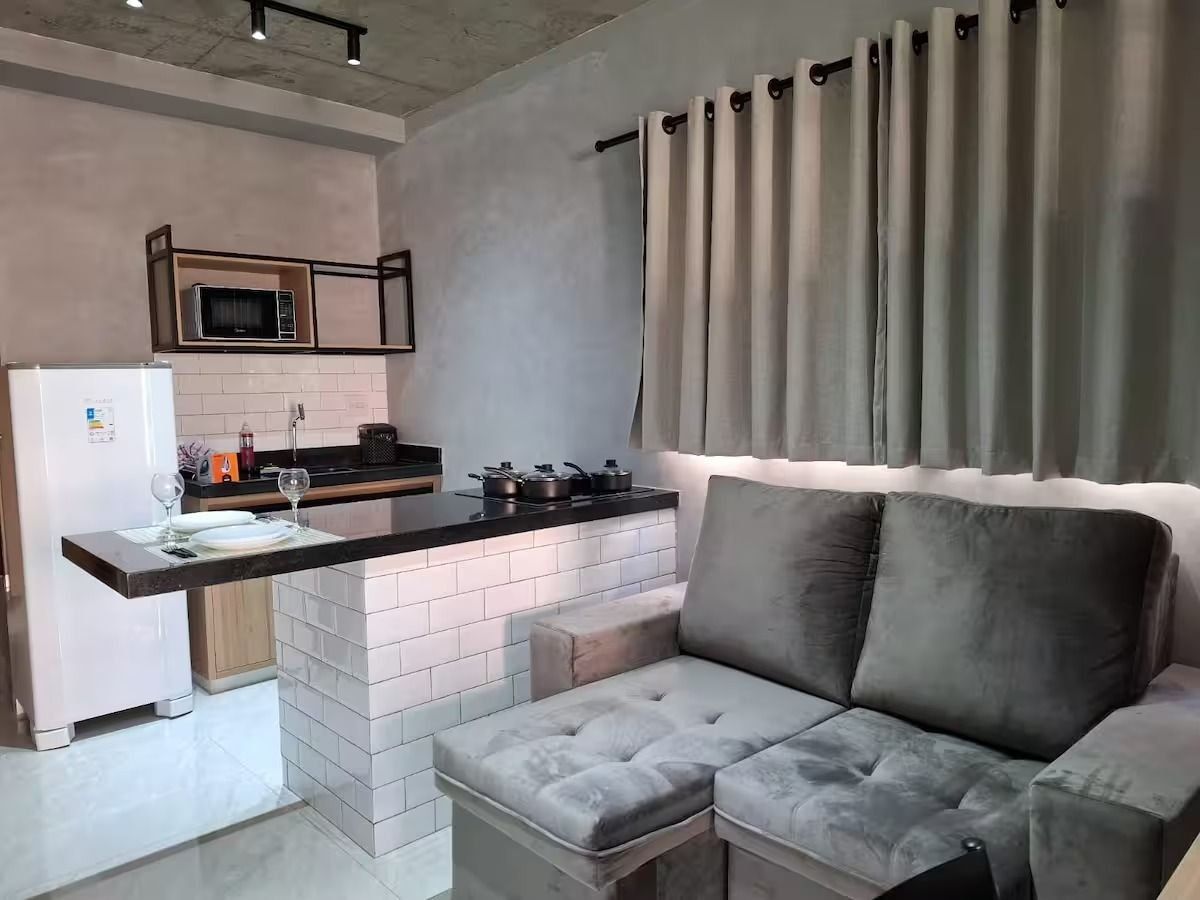 Un espacio habitable compacto con kitchenette, un sofá y un ventanal cubierto por una cortina.
