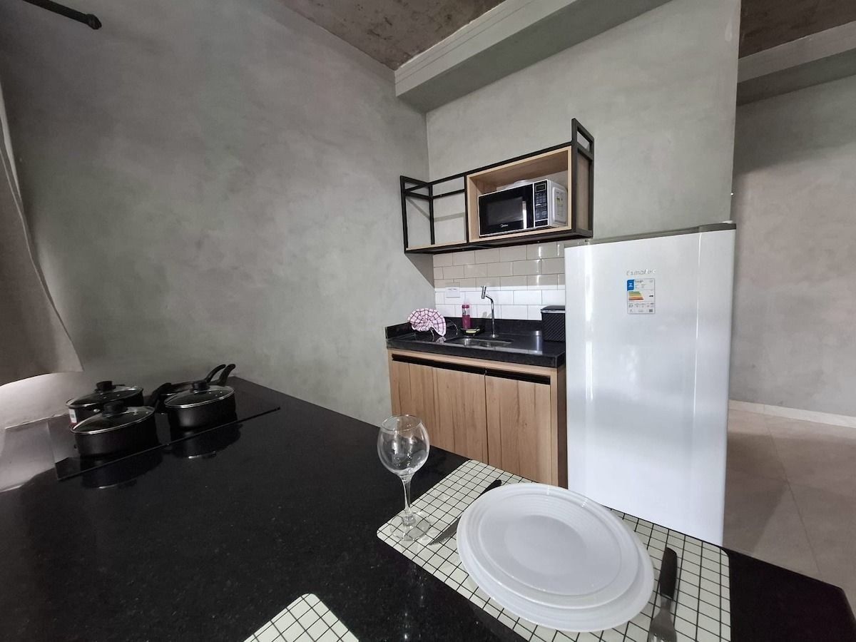 Una cocina compacta con encimera negra, refrigerador blanco, microondas y armario de madera.