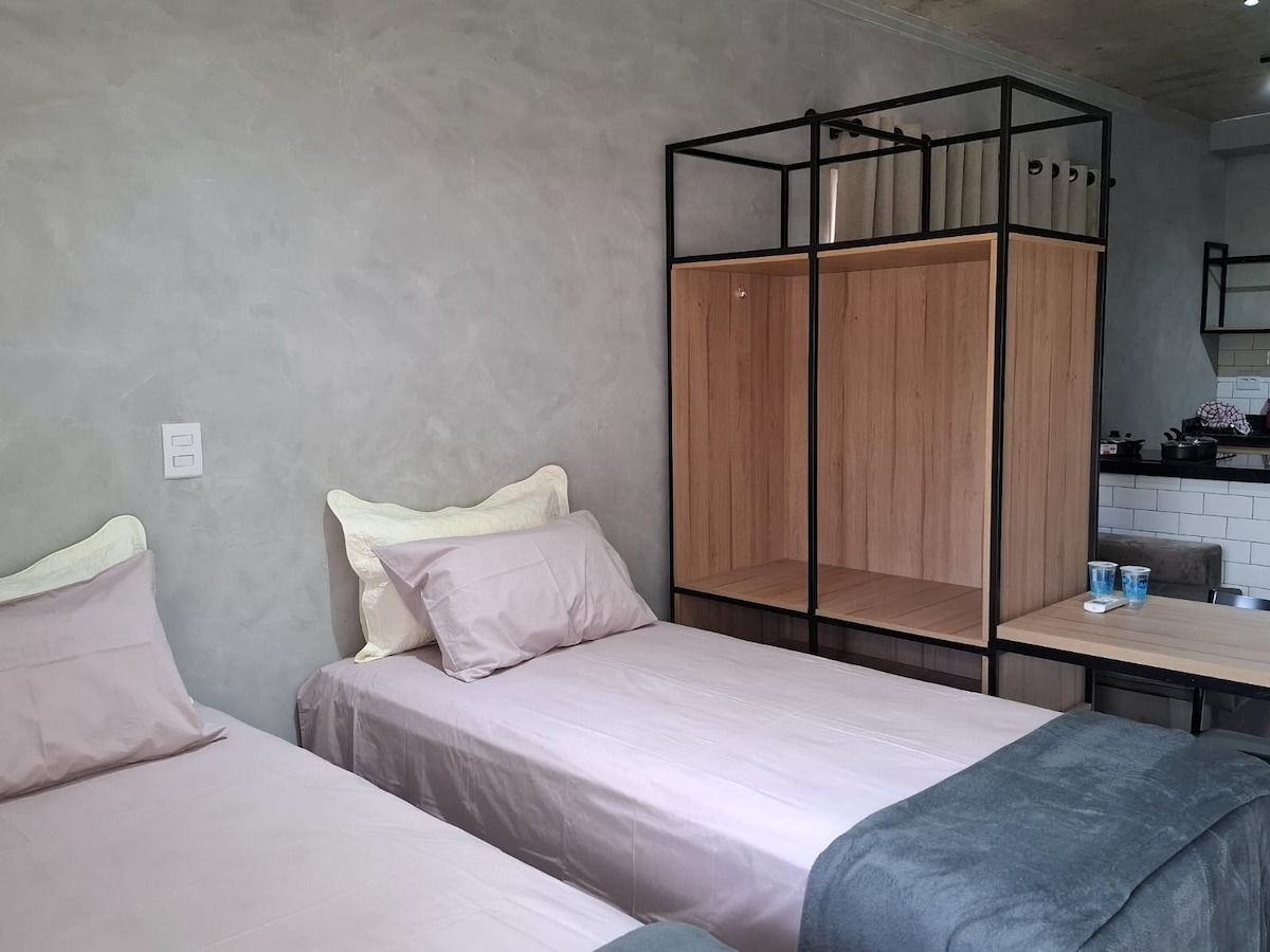 A room with two beds, a wooden wardrobe, and a small kitchenette.