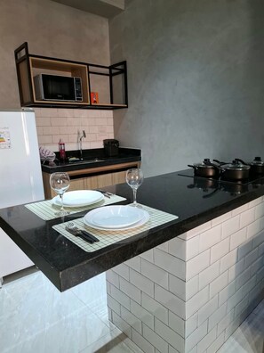 A modern kitchen with a black countertop, white tiles, a microwave, and a stove. - Edifício 1139 (São José do Rio Preto)