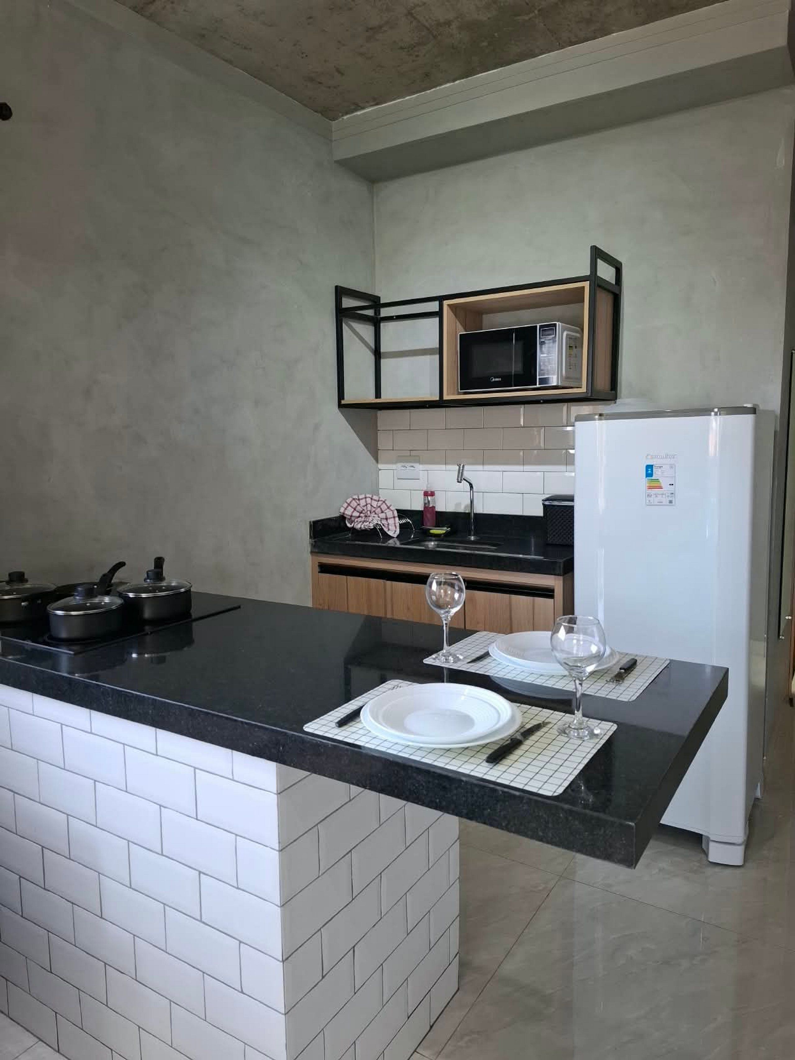 Cozinha moderna com bancada preta, painel de azulejos brancos e micro-ondas embutido.