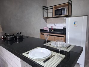 A kitchen with a black countertop, white cabinets, a microwave, and a refrigerator. - Edifício 1139 (São José do Rio Preto)