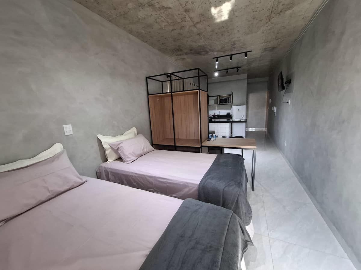 Una habitación pequeña con dos camas, un kitchenette y una mesita.