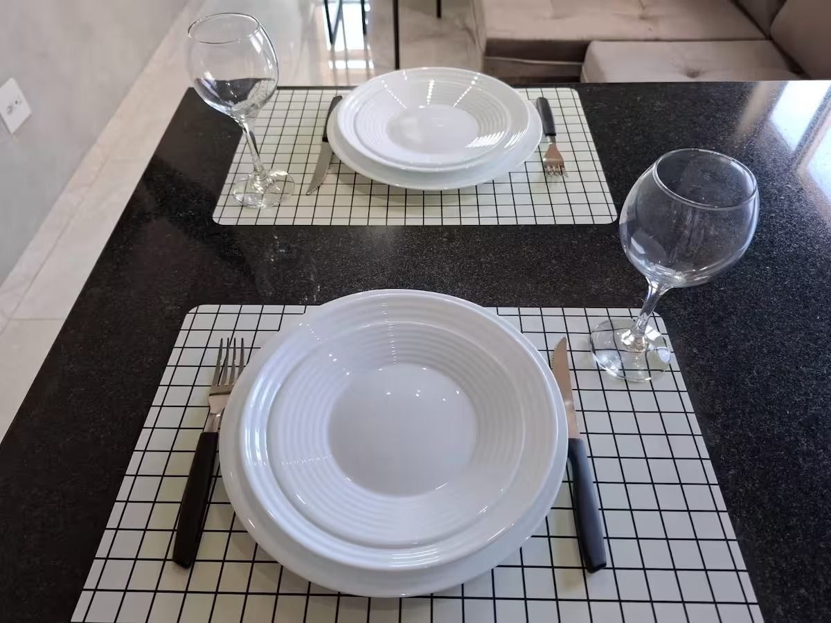 Una mesa de comedor dispuesta con platos, cubiertos y una copa de vino sobre una superficie de baldosas.