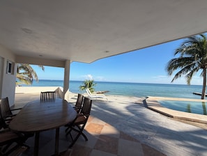 Un espacio al aire libre techado con piscina, una mesa de comedor con sillas y vistas al océano.