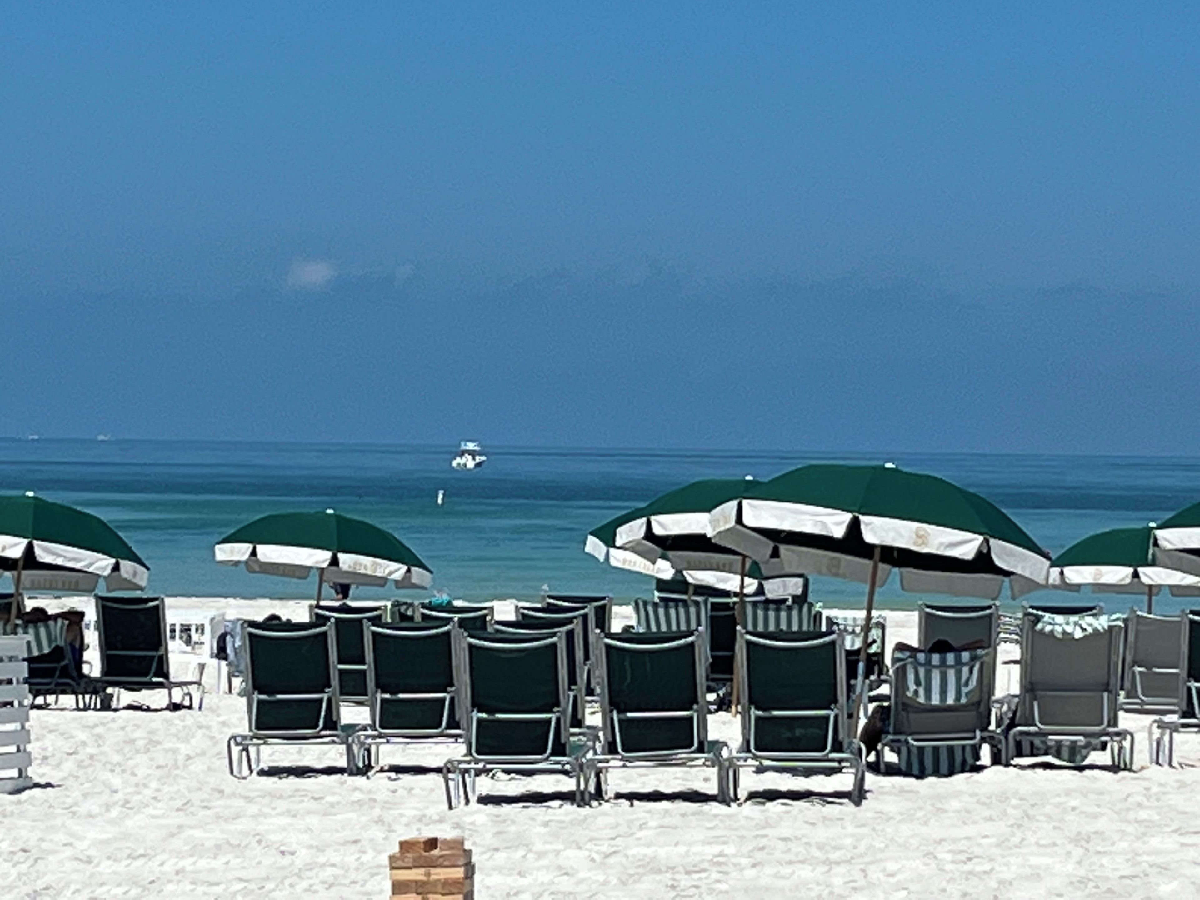 A beach with rows of sun loungers and umbrellas, a clear sky, and a boat in the distance.