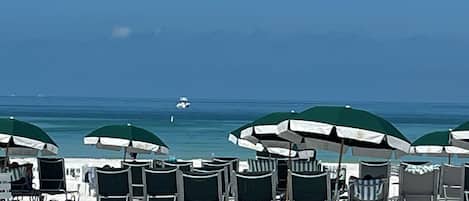A beach with rows of sun loungers and umbrellas, a clear sky, and a boat in the distance.
