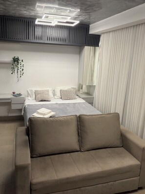 A modern bedroom with a bed, bedside tables, a hanging plant, and a sofa. - Luxury apartment | Goiânia | ID Vida Urbana Beautiful view, with comfort and elegance. (Goiânia)