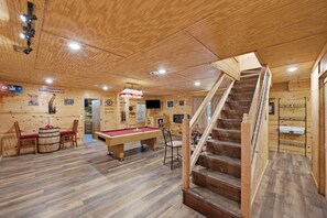 Ein Holzinterieur mit Billardtisch, Stühlen, einer Treppe und einem Fernseher.