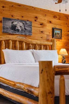 Ein Bett mit Holzrahmen, weißer Bettwäsche, einem Bärenbild darüber und einer kleinen Lampe auf dem Nachttisch.