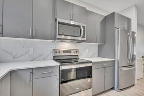 A modern kitchen with grey cabinetry, a stainless steel refrigerator, a built-in oven, and a microwave. - Modern 1BR + Den | Near West Edmonton Mall (Edmonton)