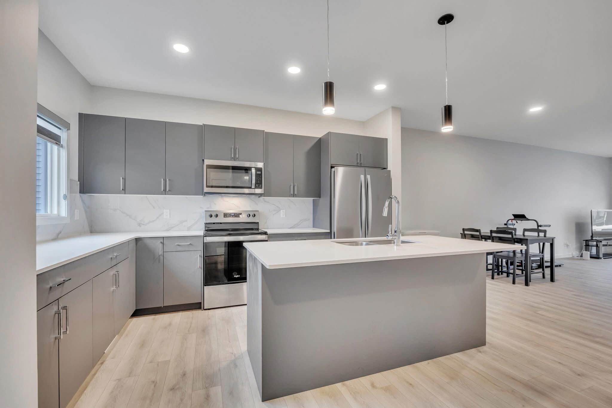 A modern kitchen with grey cabinets, stainless steel appliances, and a central island.