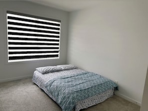 Ein kleines Schlafzimmer mit einem Bett, einem Fenster mit Jalousien und einem Teppichboden.