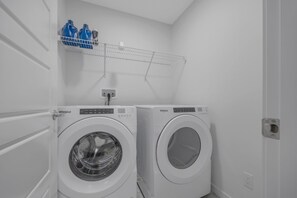 Ein Waschraum mit zwei Whirlpool Frontlader-Waschmaschinen, einem Metallregal darüber mit Reinigungsmitteln und einer Tür links.