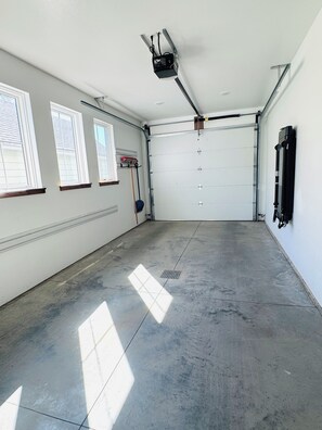 Un garaje espacioso con piso de concreto, puerta de color blanco y tres ventanas en la pared izquierda.