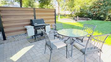 An outdoor patio with a grill, table, and chairs.