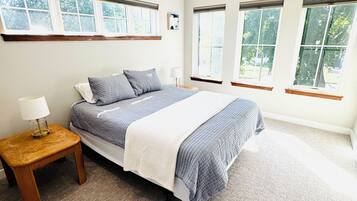 Un dormitorio con una cama grande, una mesita de noche y tres ventanas.