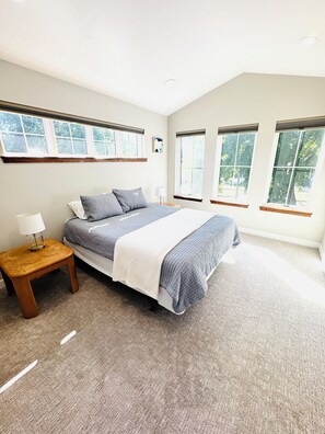 A bedroom with a large bed, a nightstand, and three windows. - New Cozy 2-Bedroom Townhome in Central Bismarck (Bismarck)