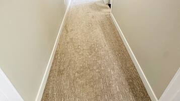 A carpeted hallway with white walls and doors, leading to another room.