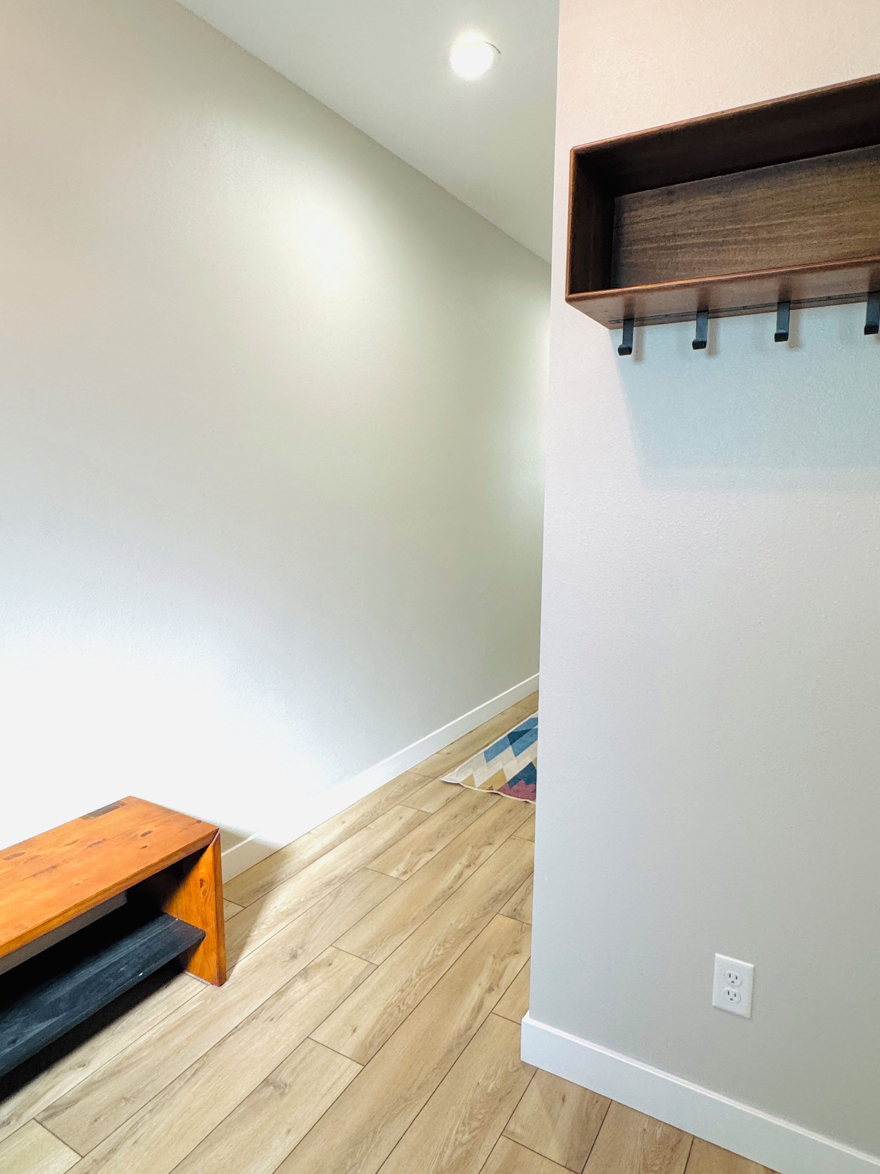 A hallway with a wooden bench, a coat rack, and a patterned rug on the floor.