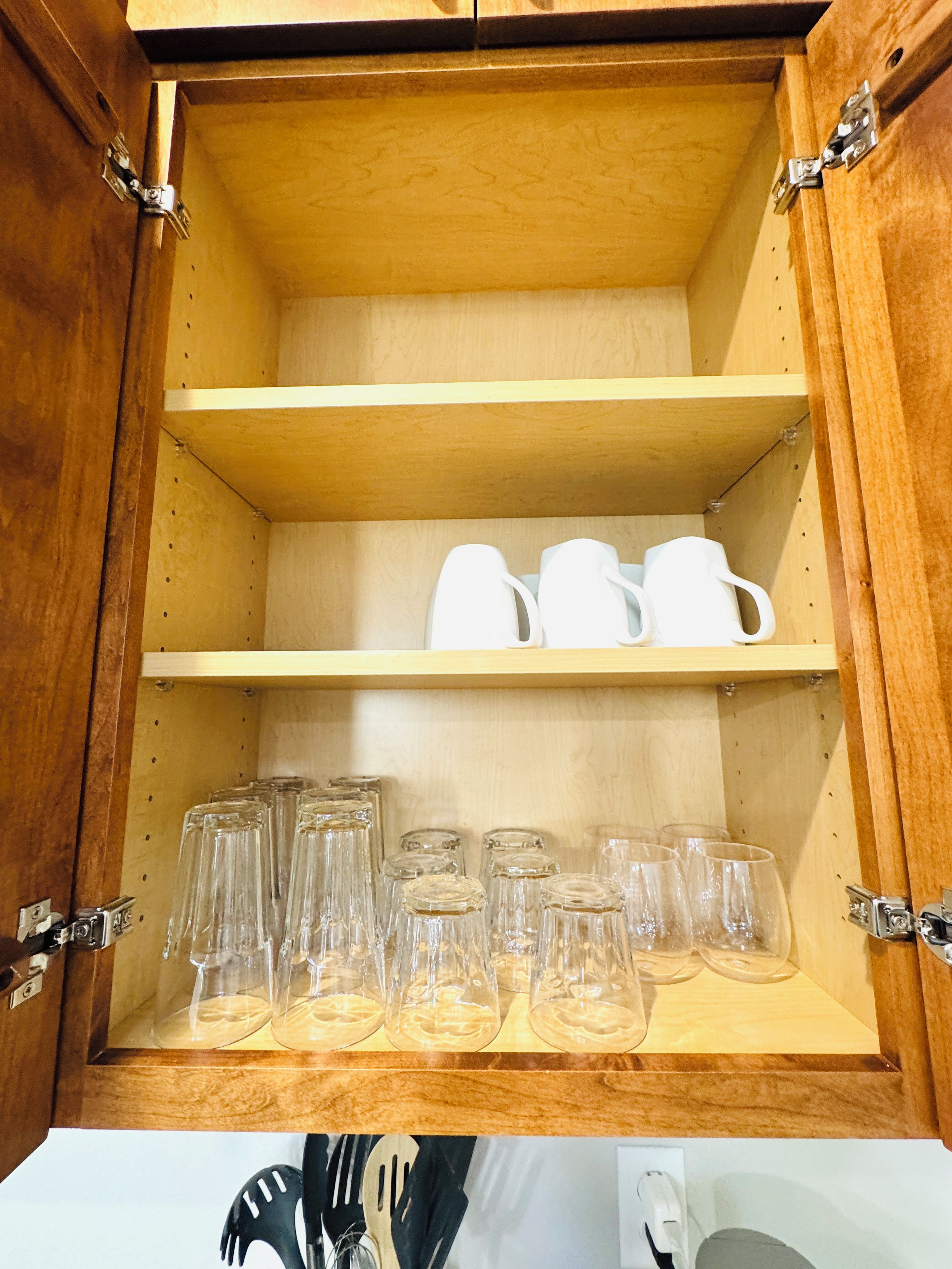 A wooden cabinet with two shelves, one holding white mugs and the other holding clear glasses.