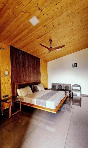 Un dormitorio con techo de madera, una cama, una mesita de noche, una silla y un ventilador de techo.