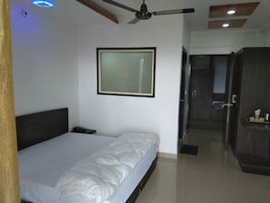 Un dormitorio con cama, ventilador de techo, un cuadro en la pared y una puerta que da a otra habitación.
