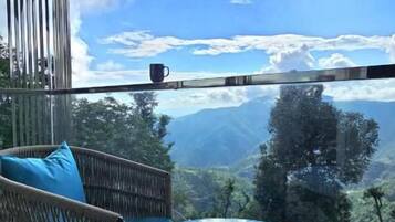 Un balcón con mesa de vidrio y mobiliario de mimbre, con vistas a un paisaje montañoso.