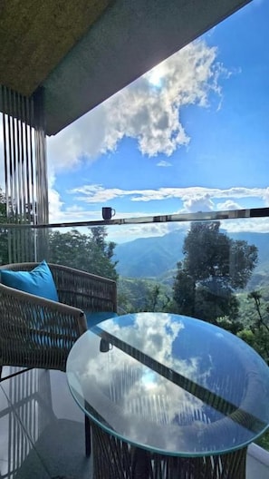 Un balcón con mesa de vidrio y mobiliario de mimbre, con vistas a un paisaje montañoso.