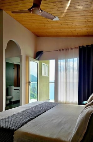A bedroom with a bed, a ceiling fan, a window with curtains, and a view of the outdoors. - Winterline Resort (Agrakhal)