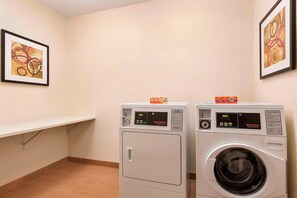 A laundry room with two front-loading washing machines and a shelf. - Fairfield Inn & Suites Houston Humble 2 Queen Std (Humble)
