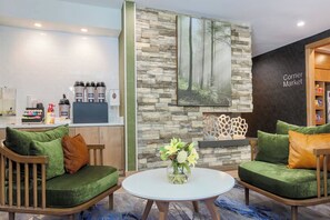 Ein moderner Wohnbereich mit zwei grünen Sofas, einer Kaffeestation und einem Waldgemälde.