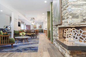 A modern hotel lobby with a stone accent wall, a fireplace, and a seating area with a blue patterned rug. - Fairfield Inn & Suites Houston Humble 2 Queen Std (Humble)