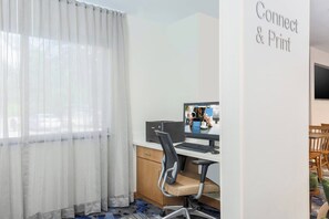 A hotel room with a desk, chair, and a computer. There is a window with sheer curtains, a wall-mounted TV, and a sign that reads 'Connect & Print'. - Fairfield Inn & Suites Houston Humble 2 Queen Std (Humble)