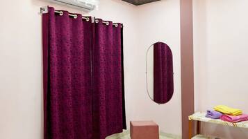 A bathroom with a shower curtain, a mirror, a small stool, and a shelf with folded towels.