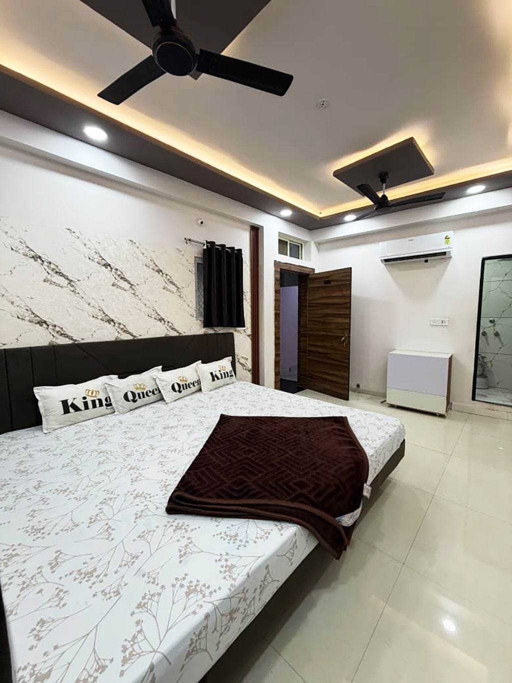 A modern bedroom with a large bed, ceiling fans, recessed lighting, and an air conditioning unit.