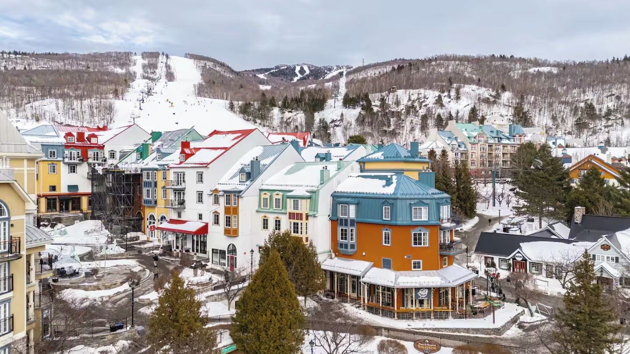 Une ville enneigée, avec des bâtiments aux couleurs vives et une piste de ski en arrière-plan.