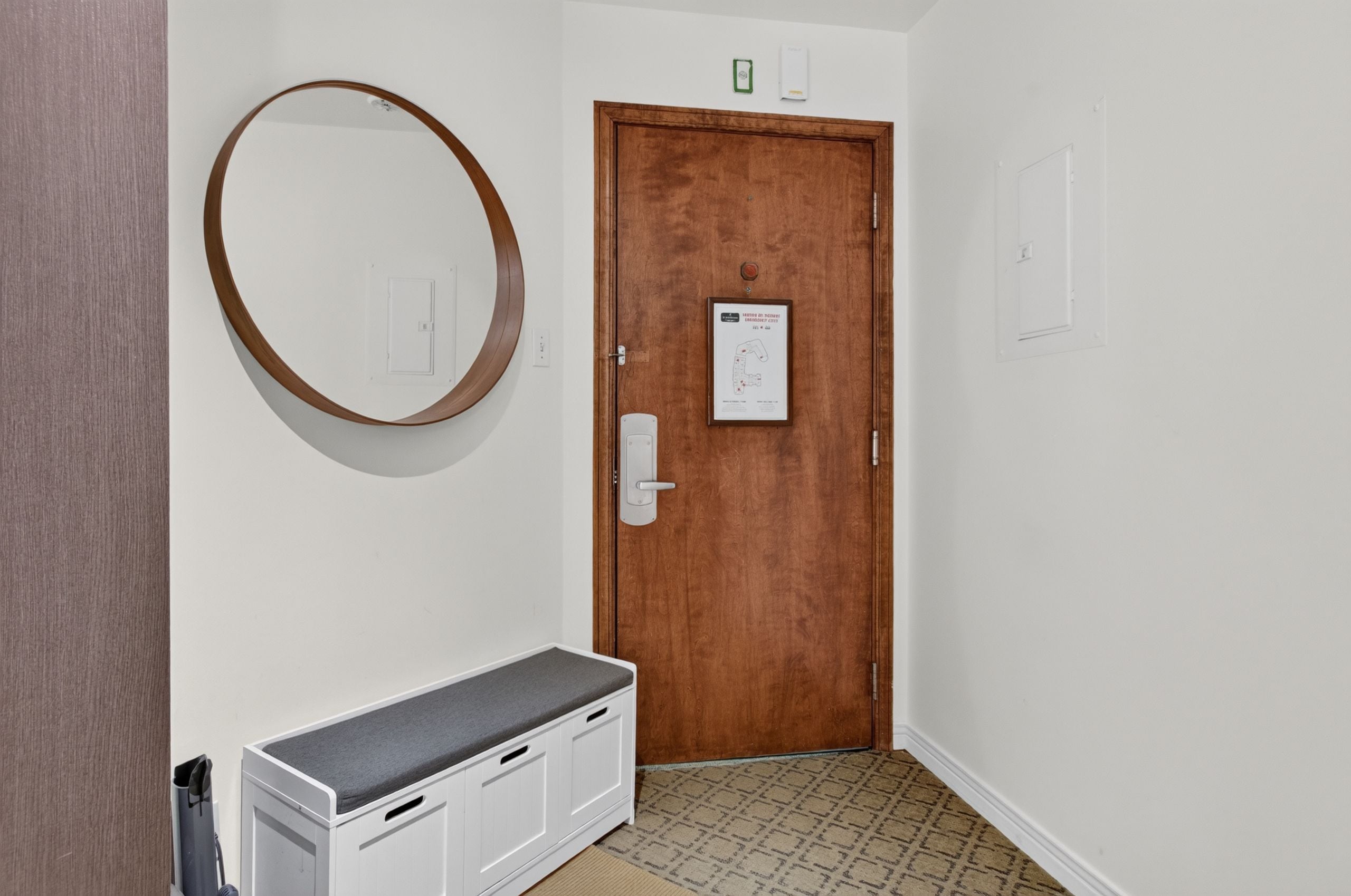 Un pasillo con una puerta de madera, un banco blanco y un espejo fijado a la pared.