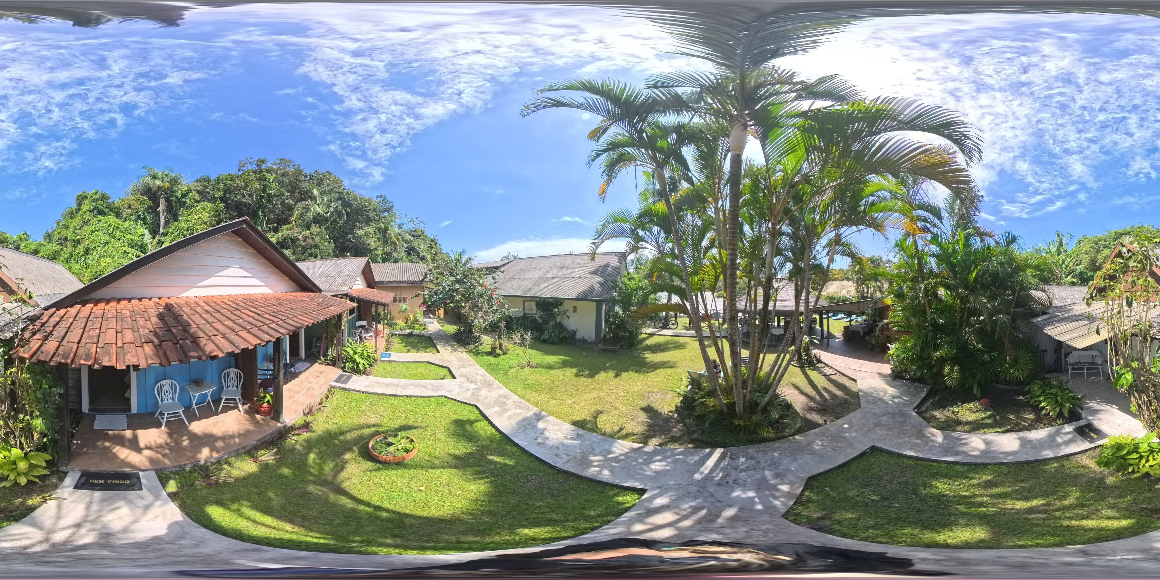 Ein tropisches Resort mit mehreren bungalowartigen Gebäuden, einer großen Rasenfläche und einer stattlichen Palme.
