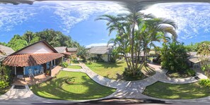 A tropical resort with multiple bungalow-style buildings, a central lawn area, and a large palm tree.