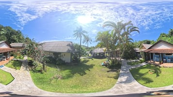 A tropical resort with multiple bungalow-style accommodations, a central gazebo, and a well-maintained lawn.