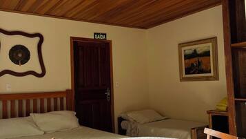 Een kamer met twee bedden, een houten plafond, een deur met de tekst 'SAÍDA', een schilderij aan de muur en een tafel met een kantkleed.