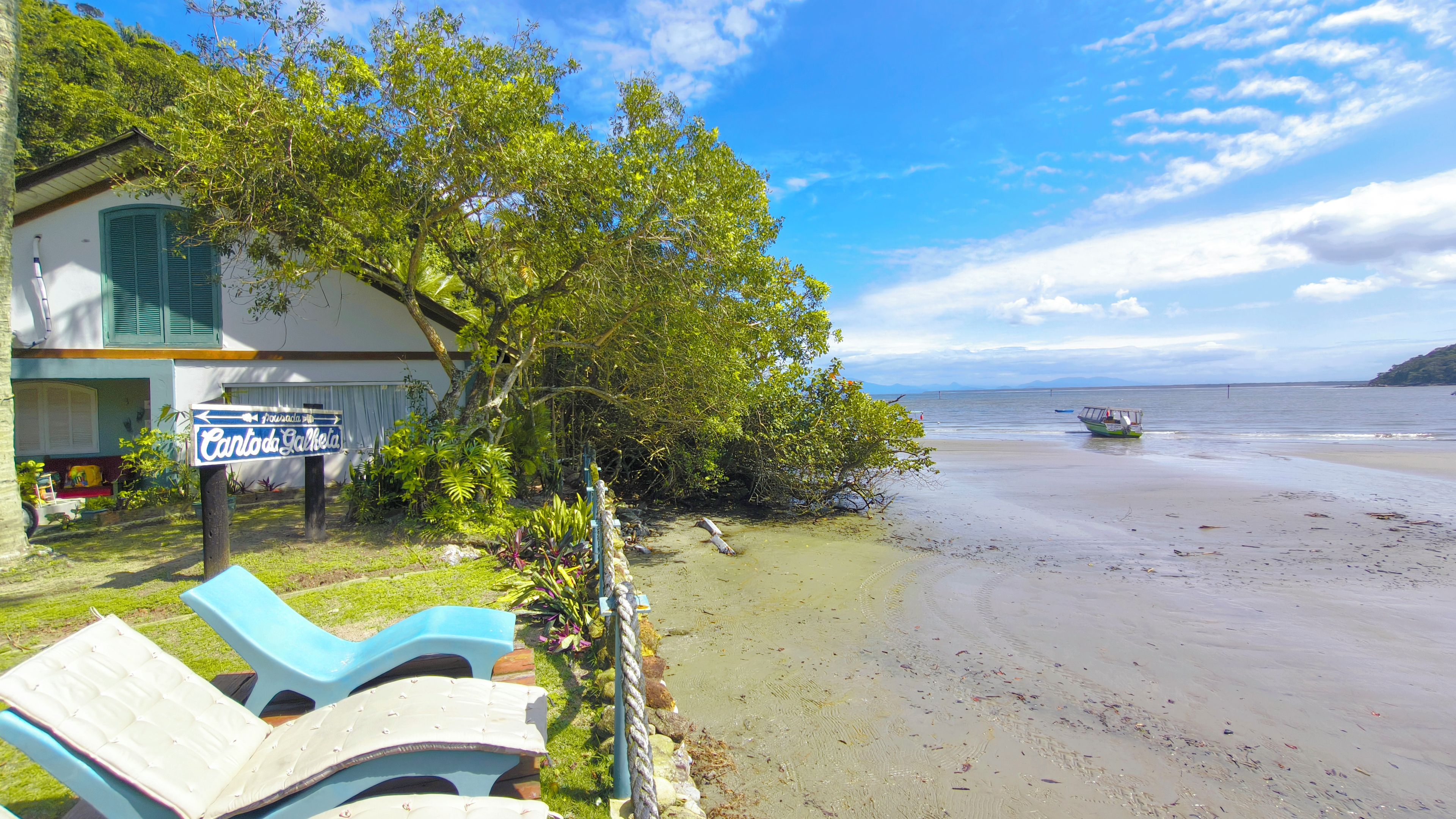 A beachfront property with a sign indicating 'Cantada Gallega,' a lounge chair, and a boat on the beach.