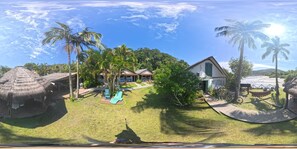 A tropical resort with thatched-roof structures, a swimming pool, and a large house with a prominent window.