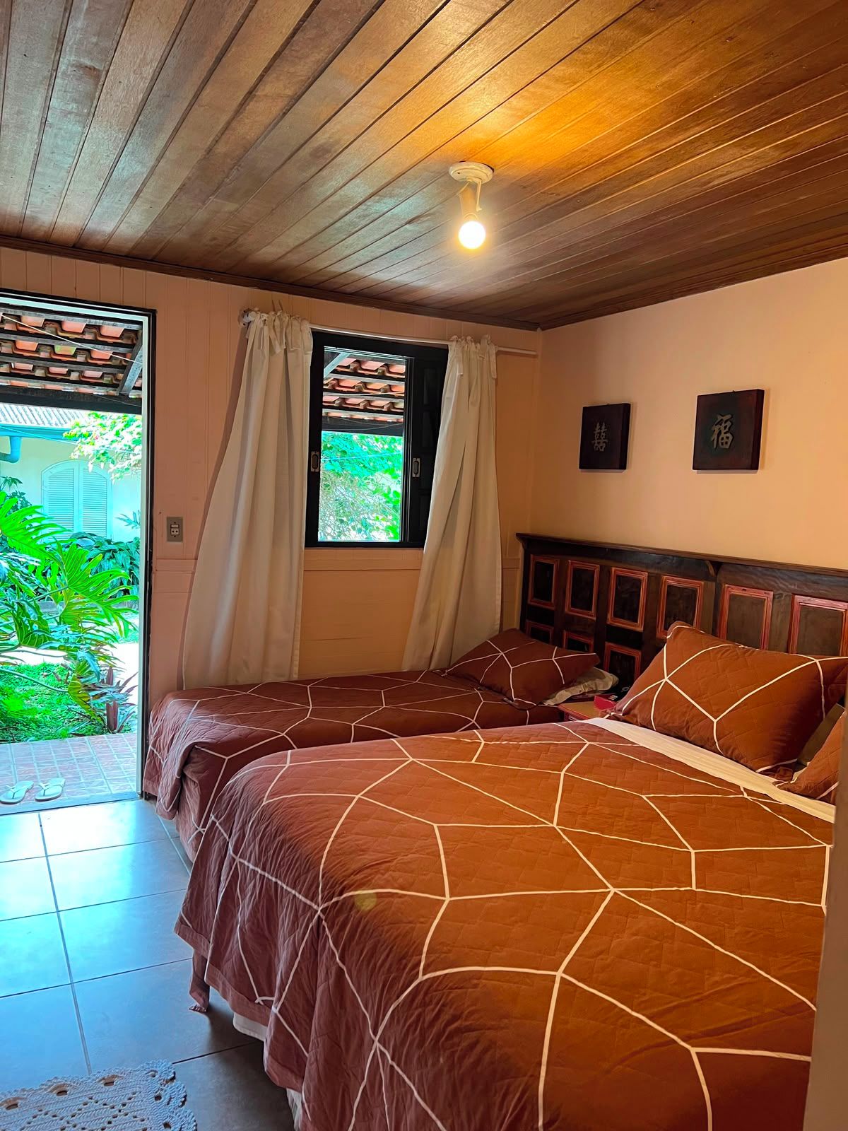A room with two beds, a window with curtains, and a ceiling light.