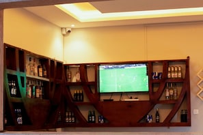 A room with a television mounted on a wooden shelf structure, surrounded by shelves containing various bottles. - Spark Africa Hotel Jinja (Jinja)
