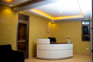 A reception desk with a glass partition, a small plant, and a framed picture on the wall. - Spark Africa Hotel Jinja (Jinja)