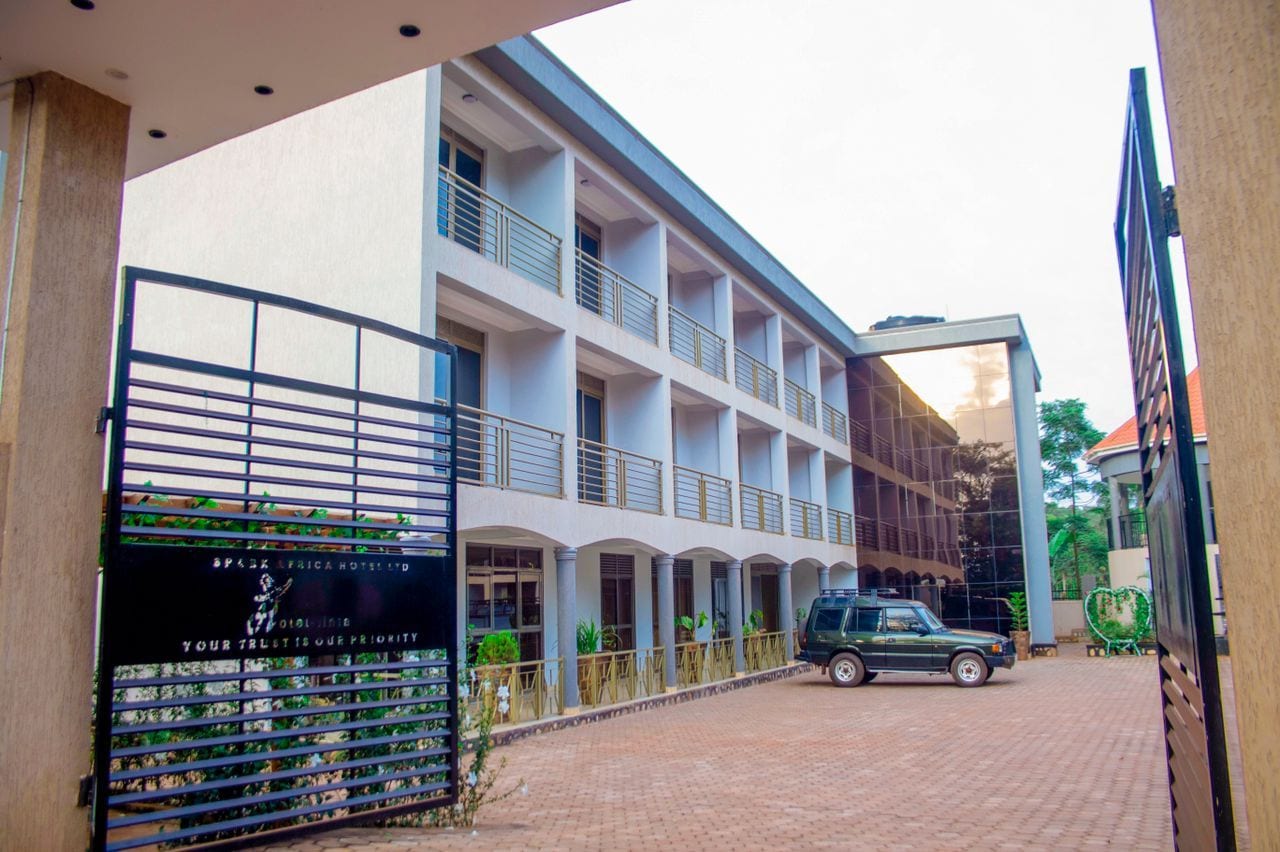 Un hotel de varios pisos con un área exterior techada, una entrada con portón y un vehículo estacionado.