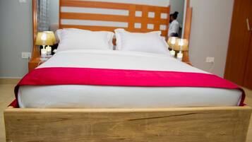 Un letto con testiera in legno, biancheria bianca e coperta rossa. Sono presenti abat-jour e uno specchio a parete.
