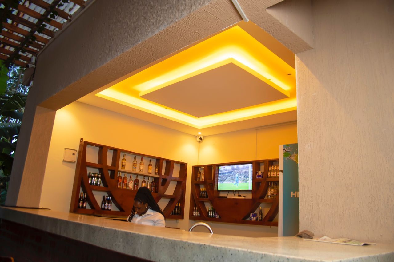 A bar area with a counter, shelves of bottles, and a television screen.